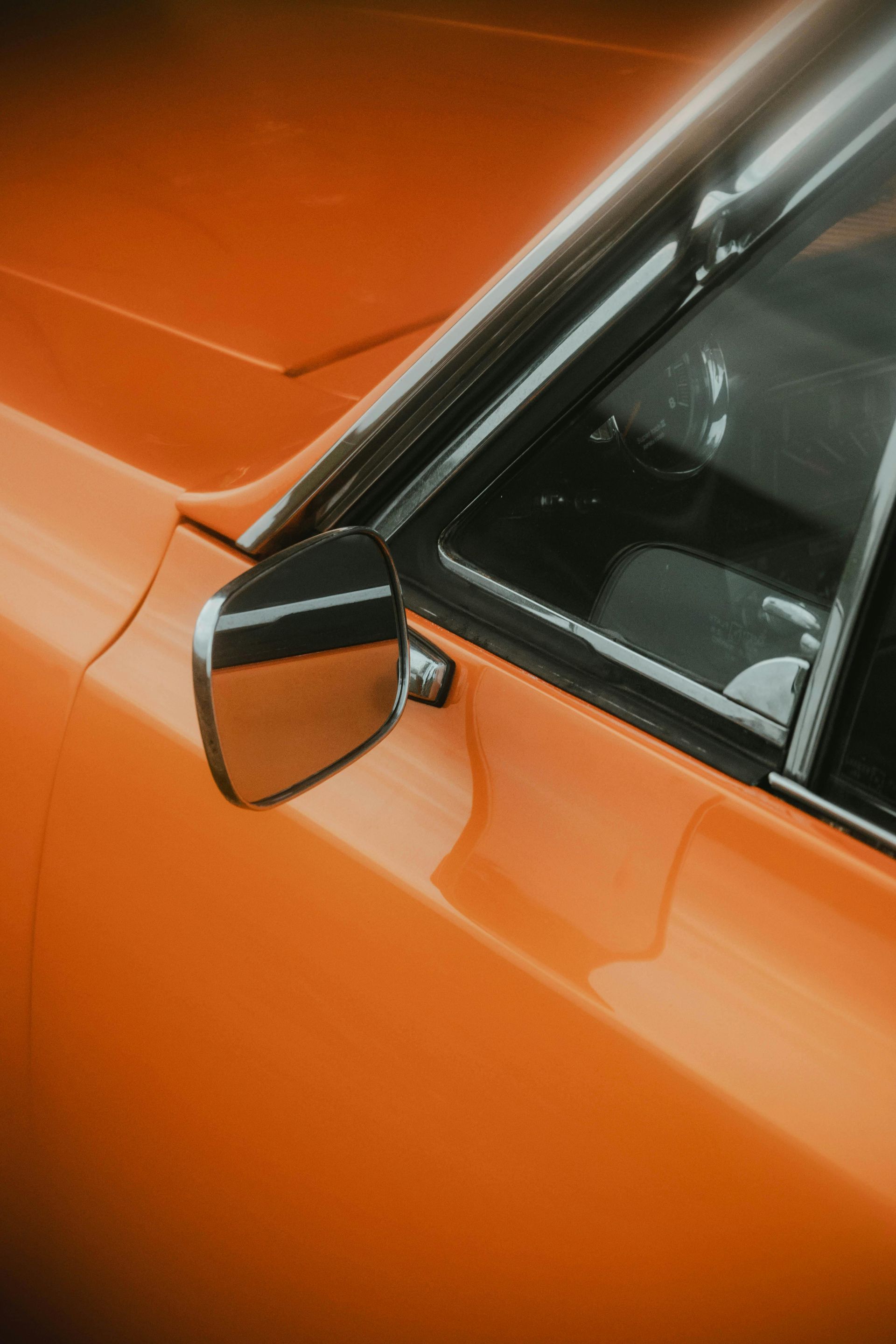 Orange classic car, side view, chrome mirror reflecting a garage.