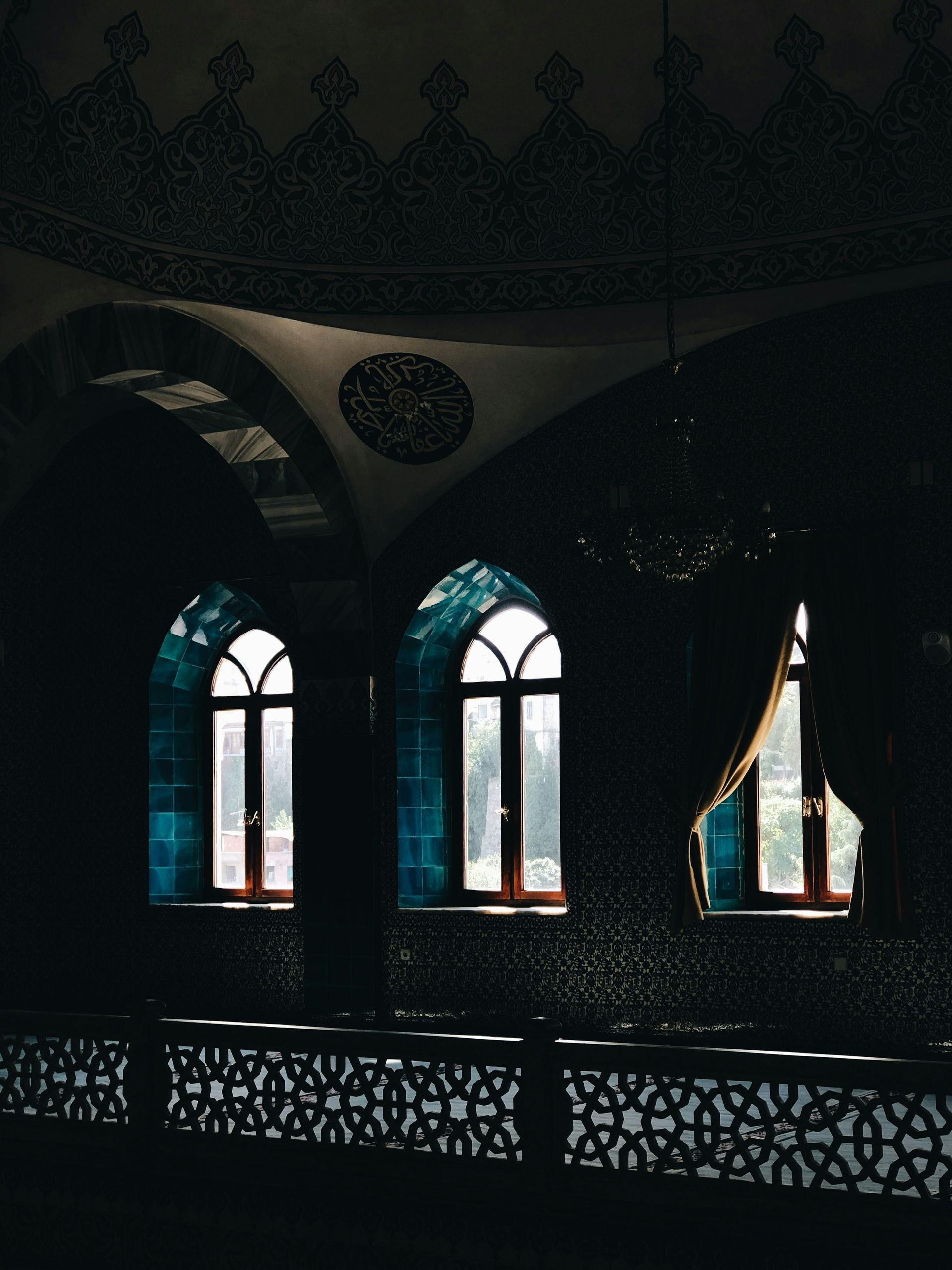 Dark interior of a mosque with arched windows, blue tiled walls, and intricate patterns.