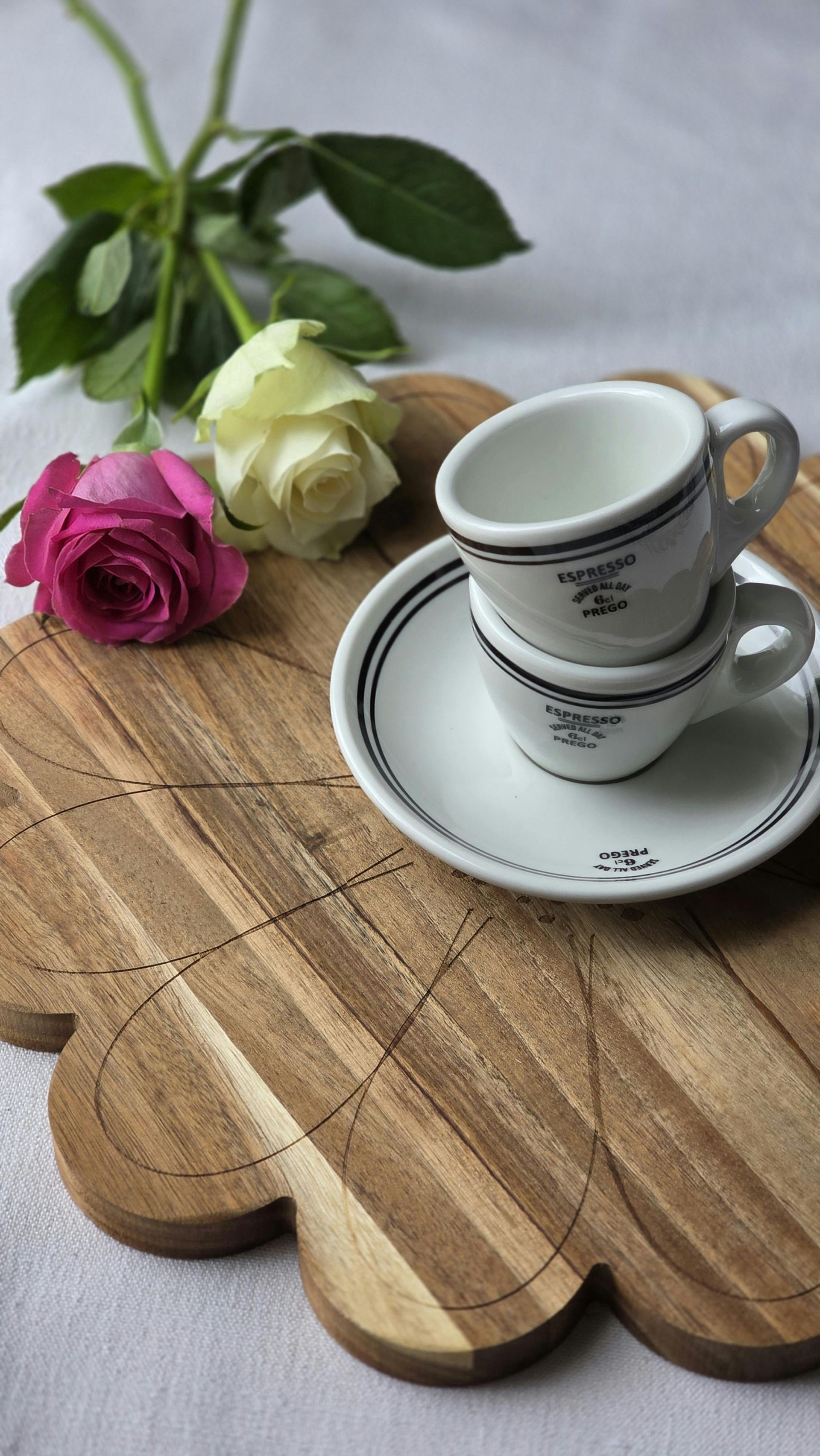 Wooden tray with stacked espresso cups and pink and white roses.