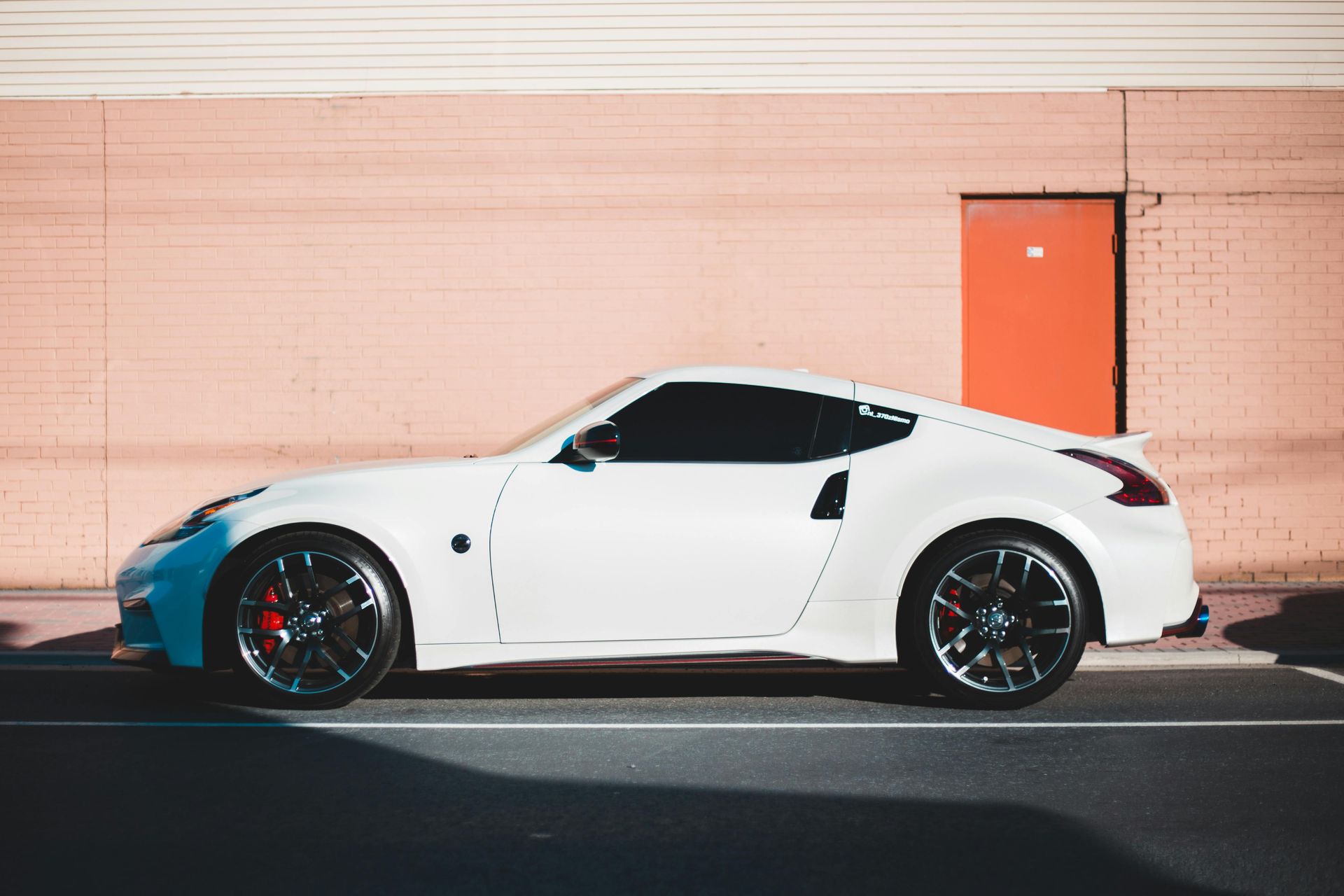 White sports car parked in front of a brick wall with a red door.