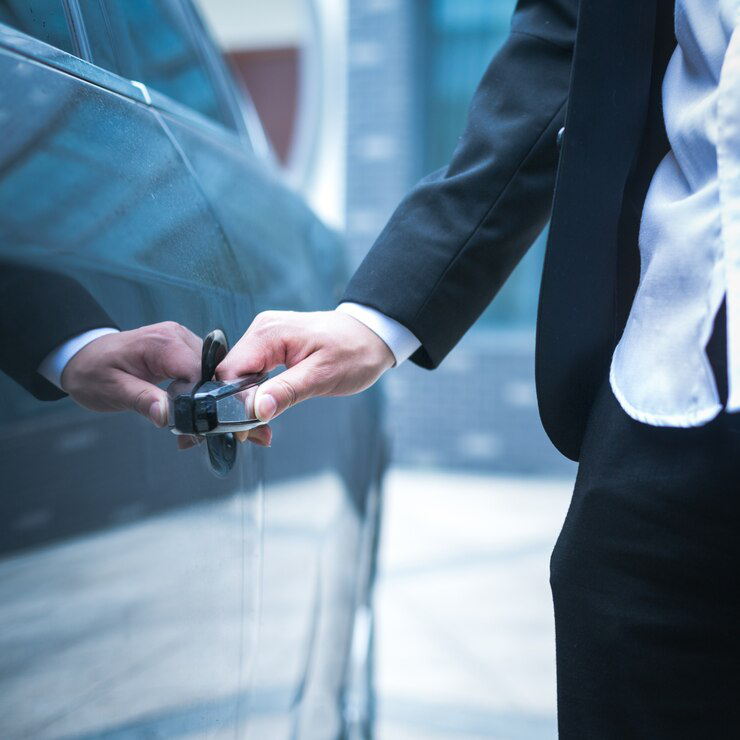 Person in a suit opening a car door, holding the handle with one hand.