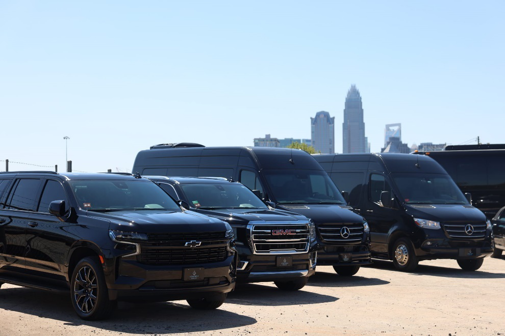 Black SUVs and vans parked in a lot, city skyline in the background.