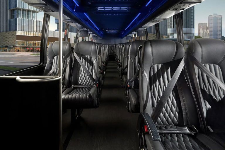 Interior of a bus with rows of black and orange seats, orange curtains, and overhead storage compartments.