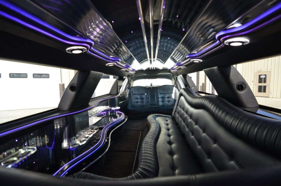 Interior of a limousine with black leather seating, a bar, and blue ambient lighting on the ceiling.