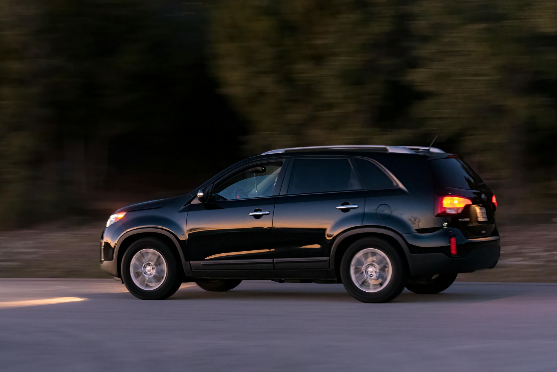 Black SUV driving on a road with trees in the background, daytime.
