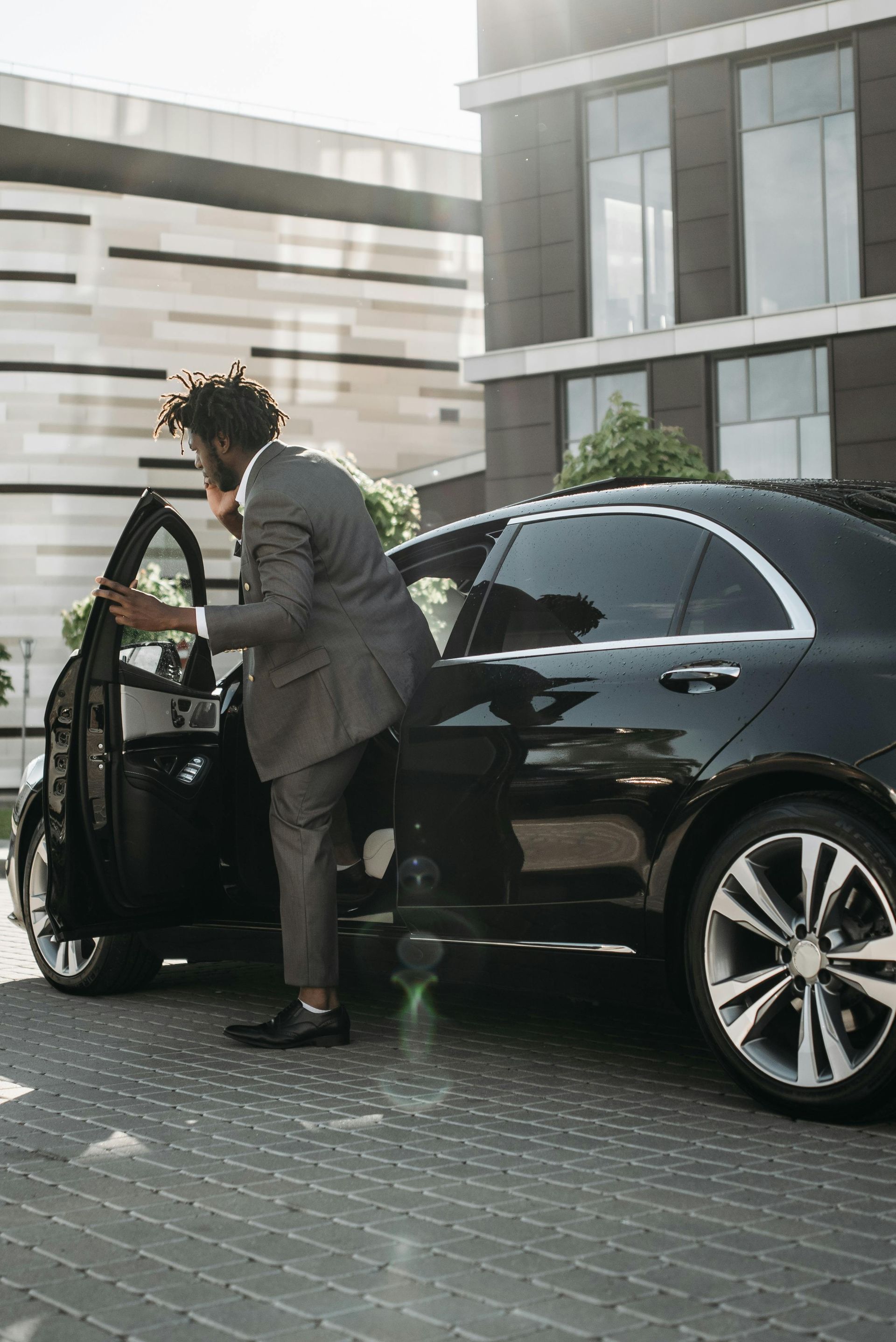Man in suit exiting a black car in front of a modern building.