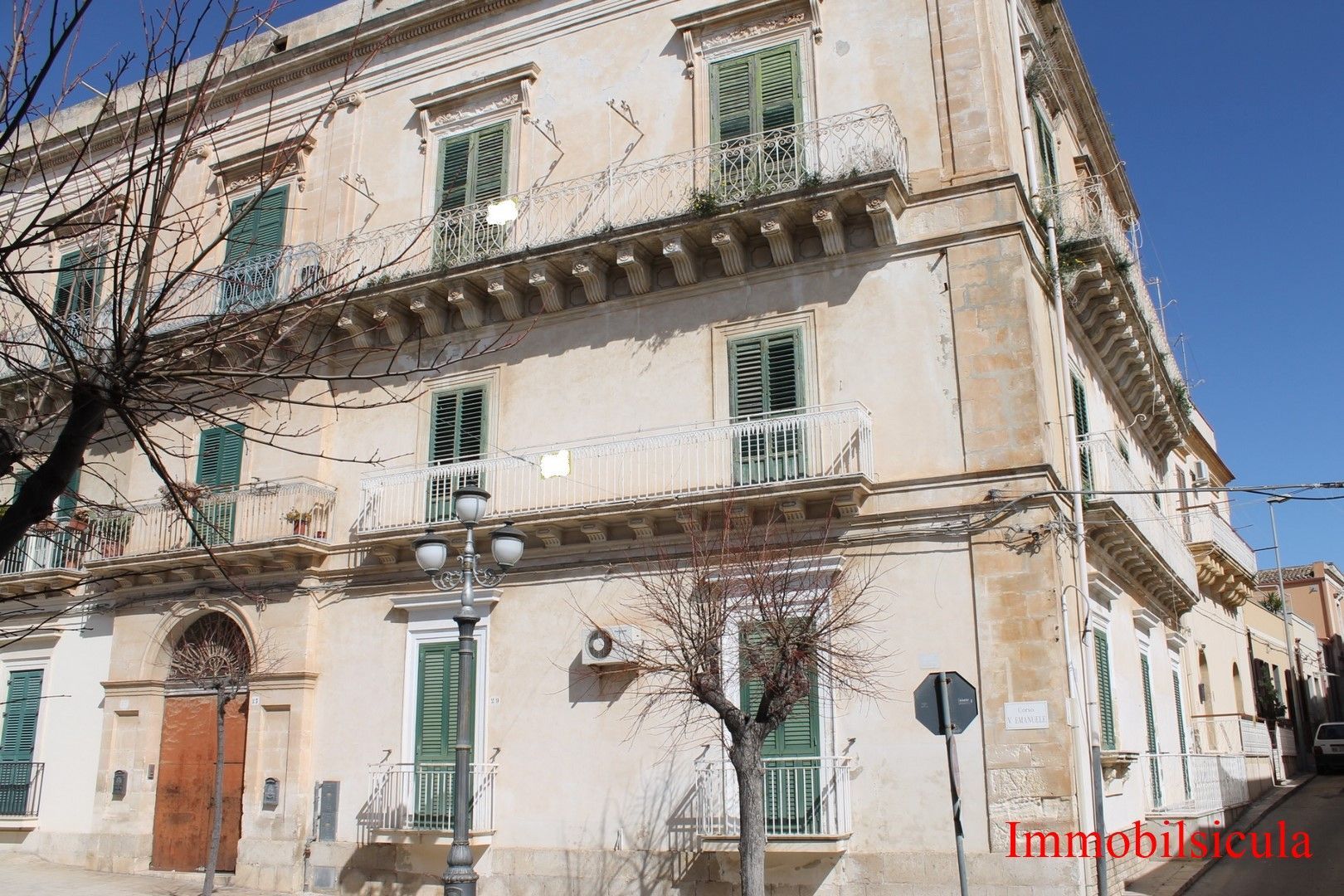 Vecchio edificio d'angolo soleggiato con persiane verdi e balconi su una strada stretta