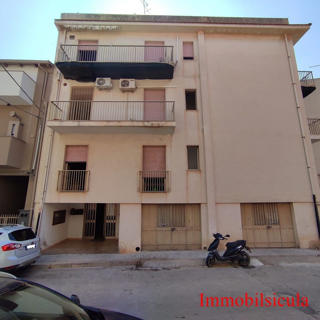 Edificio residenziale beige a tre piani con balconi, scooter parcheggiato e auto in strada.