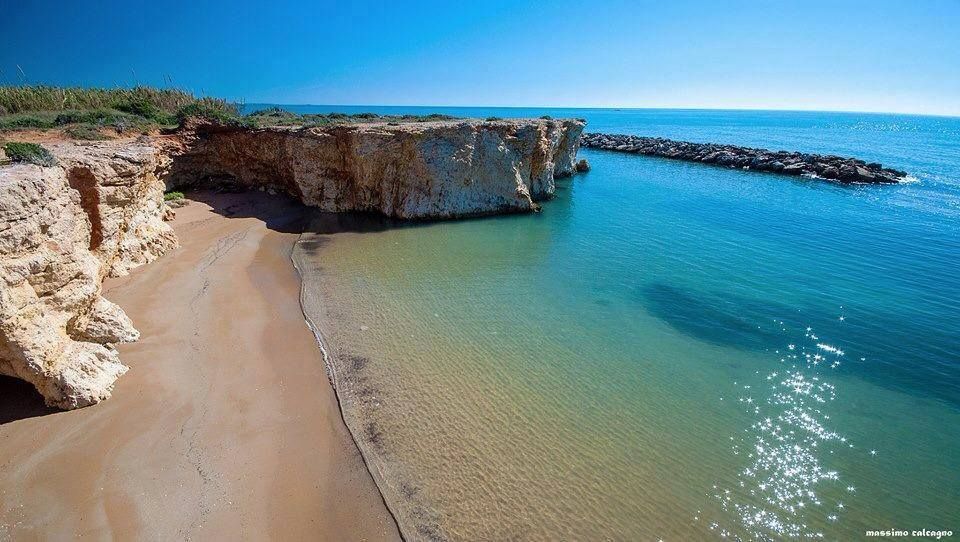 Caletta sabbiosa con acqua turchese, scogliere rocciose e un cielo azzurro limpido.