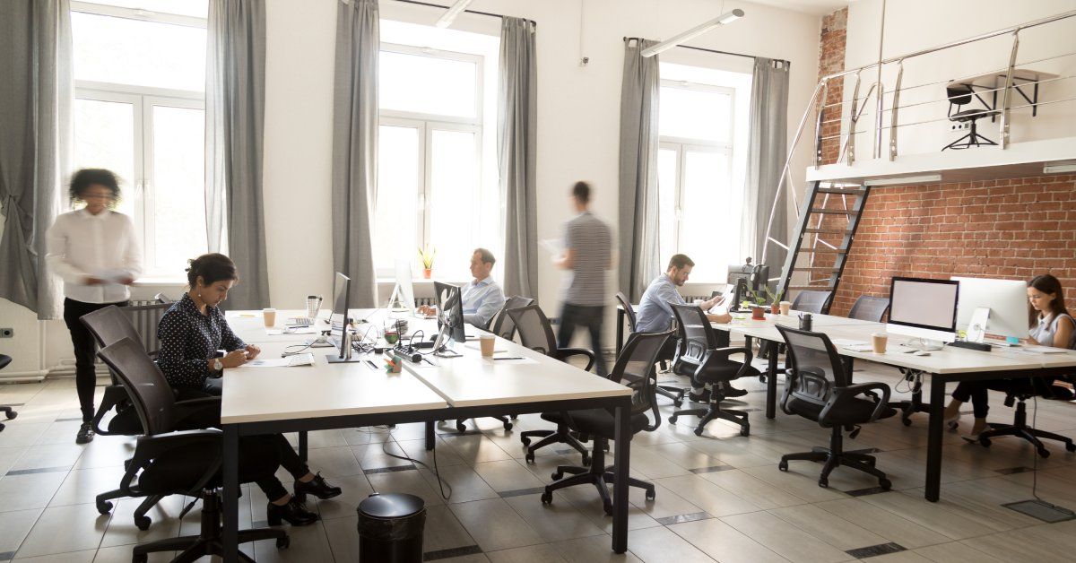 A large, open flex space office filled with tables, computers, and several employees working.