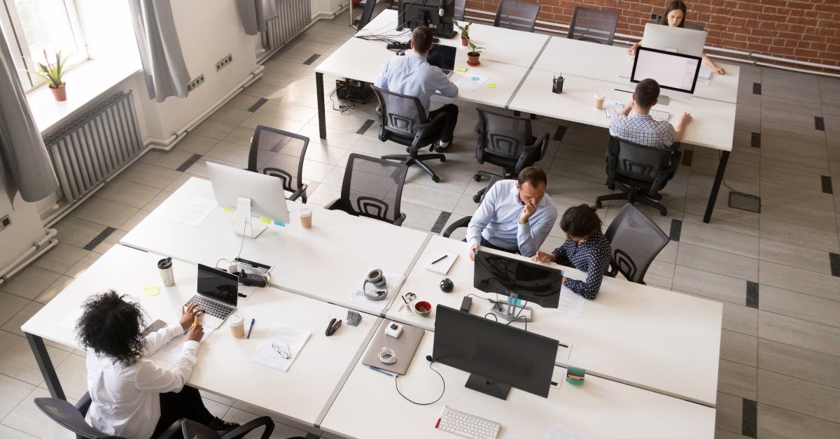 Angled birds-eye-view of a shared office space with several tables, computers, and employees working together.