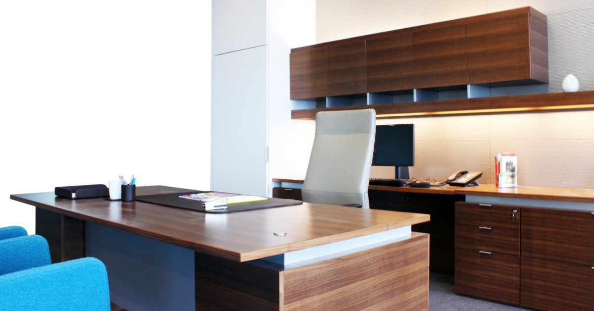 A private office space with dark wood cabinets, a large desk, an office chair, a computer, and two blue chairs.