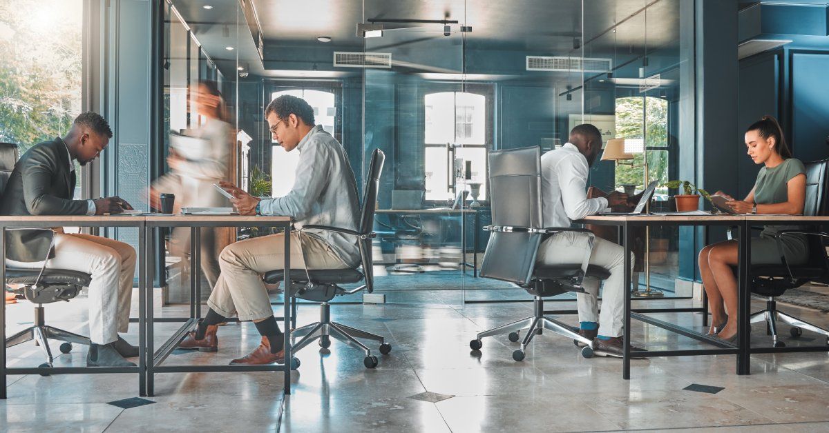 A large shared office space with tile floors, several desks, and multiple employees sitting and working.