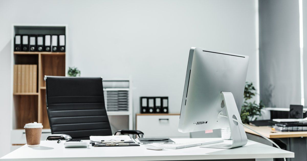 A private office space with a desk, computer, black chair, and shelves and cabinets in the background.