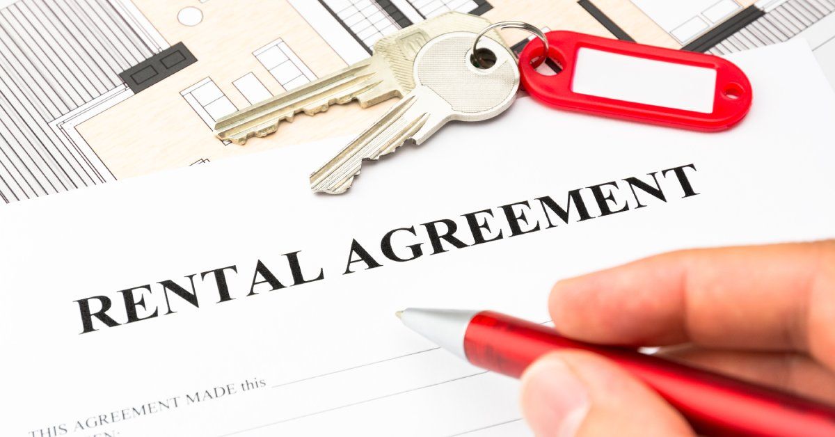 Closeup of a hand signing a rental agreement document with a red pen and a set of keys on the table.