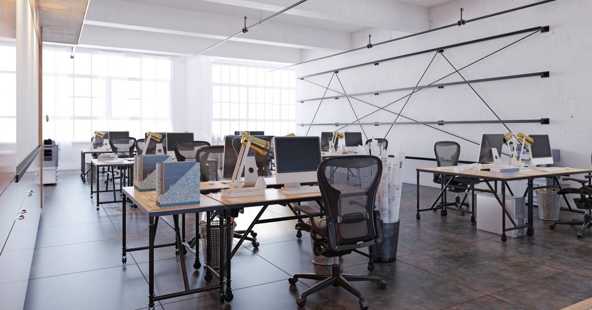 A modern office space with white walls, large windows, and an open layout with several desks and work stations.