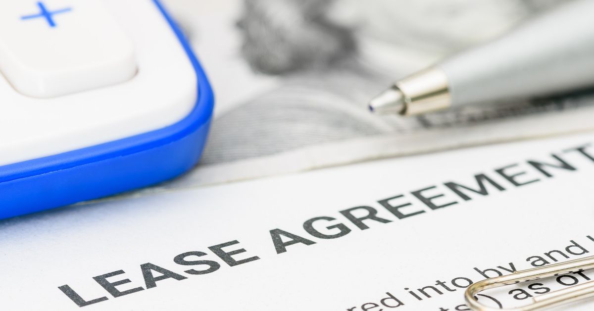 Closeup of a stack of documents that says “lease agreement” next to a pen, paper clips, and a calculator.