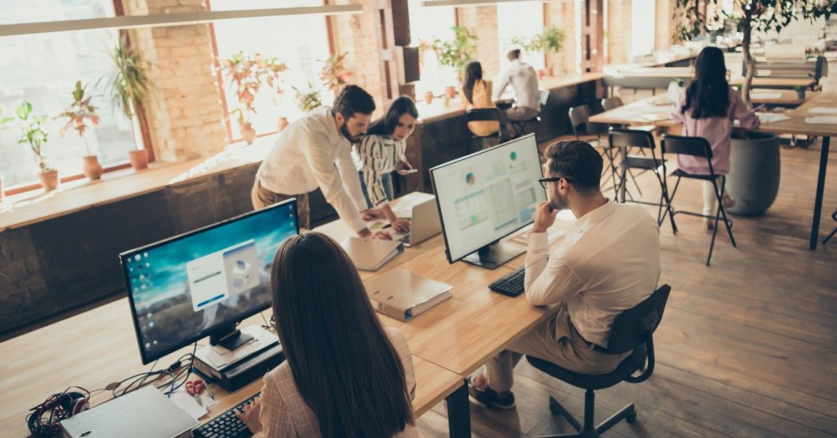 Several people are sit at different desks in a shared work space. Some desks have computers on them.
