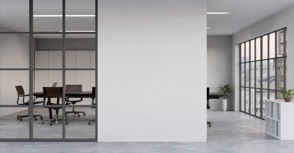 A conference room hidden behind a large white wall with a long table and black swivel chairs surrounding it.