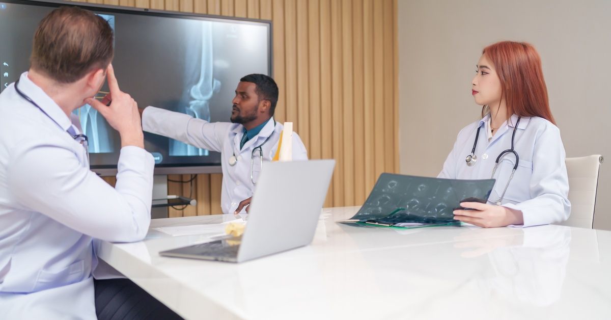 A group of three medical professionals looking at the x-rays of a person's arms in a conference room with a white table.