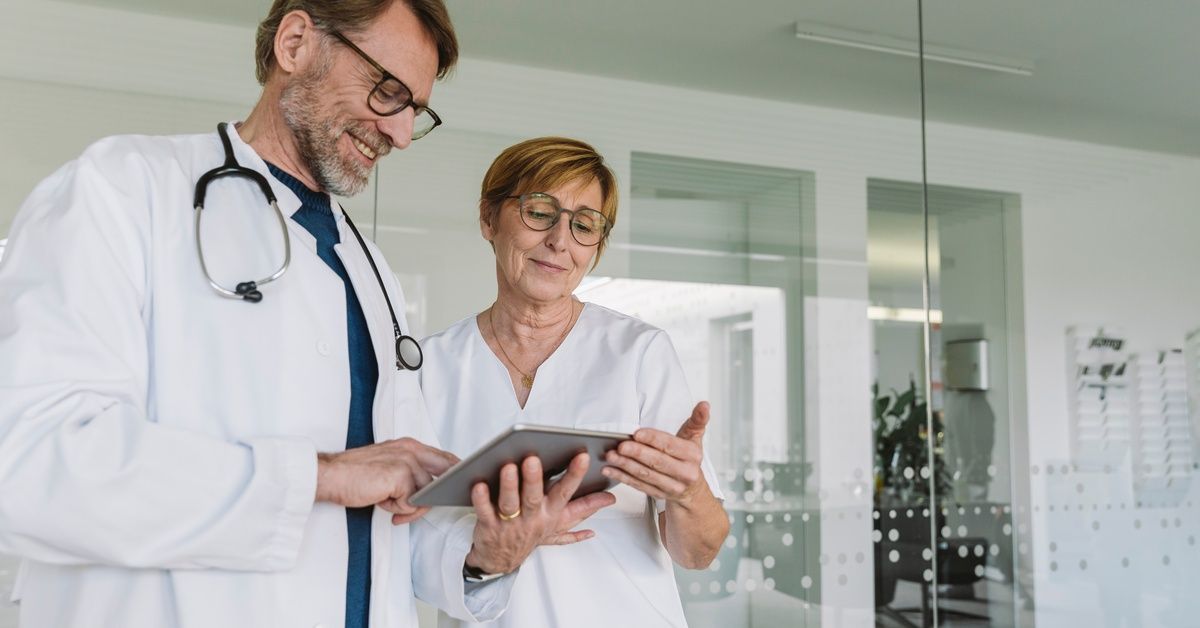 Two medical professionals looking over the contents of a digital tablet in a room with glass walls.