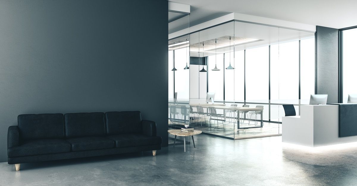 An office reception area with a modern theme that includes polished concrete flooring, a black couch, and large windows.