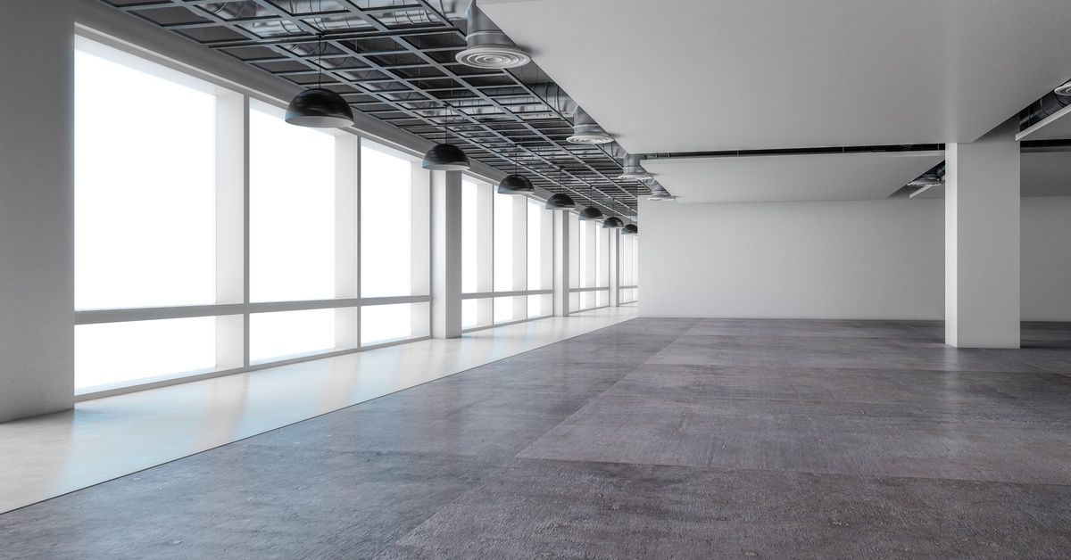 An empty office space with a long hallway, black pendant lights, dark hardwood floors, and windows.
