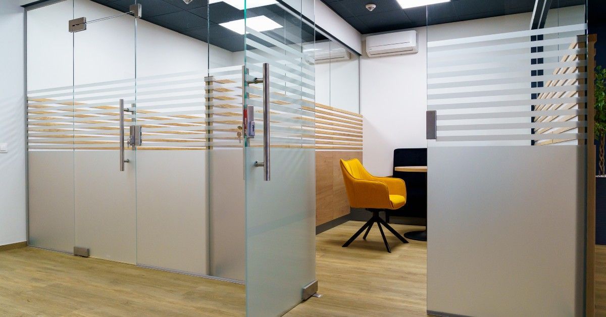 Two closed-off office cubicles with glass doors. One open door reveals a yellow chair next to a desk.