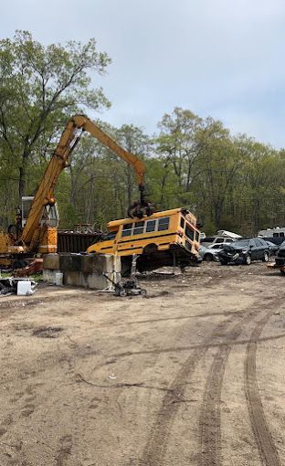 A yellow school bus is being lifted by a crane in a scrap yard.