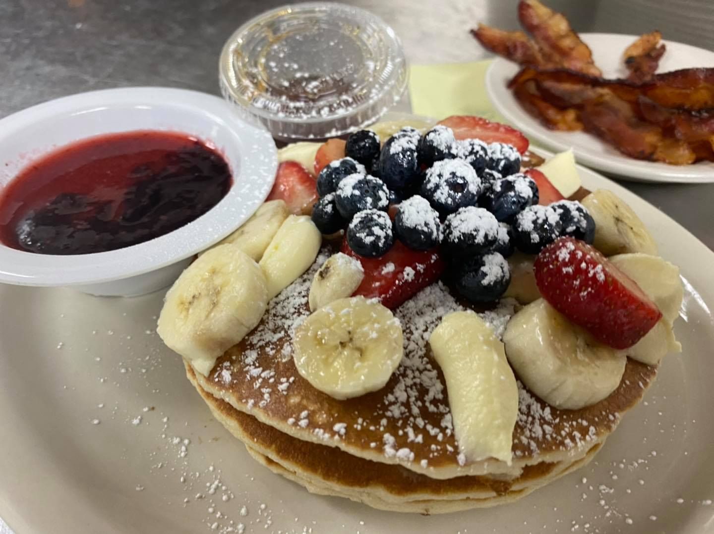 Pancakes with fruit and berry compote, bacon, and syrup.