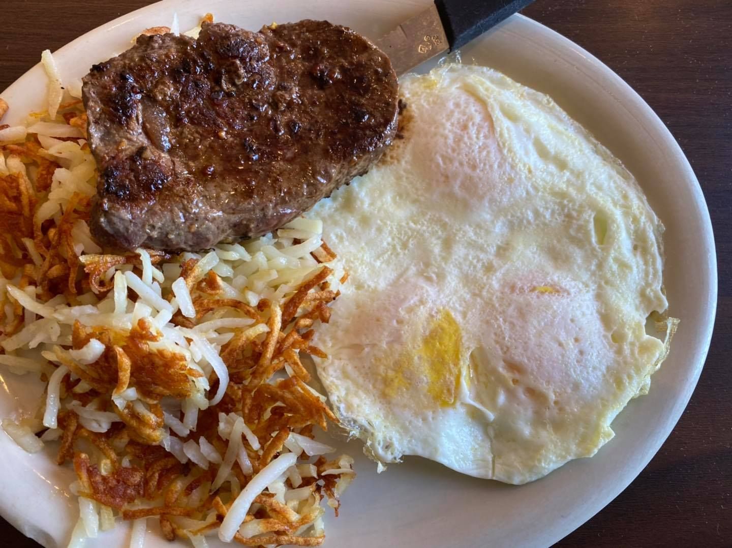 Breakfast plate with steak, hash browns, and three fried eggs.