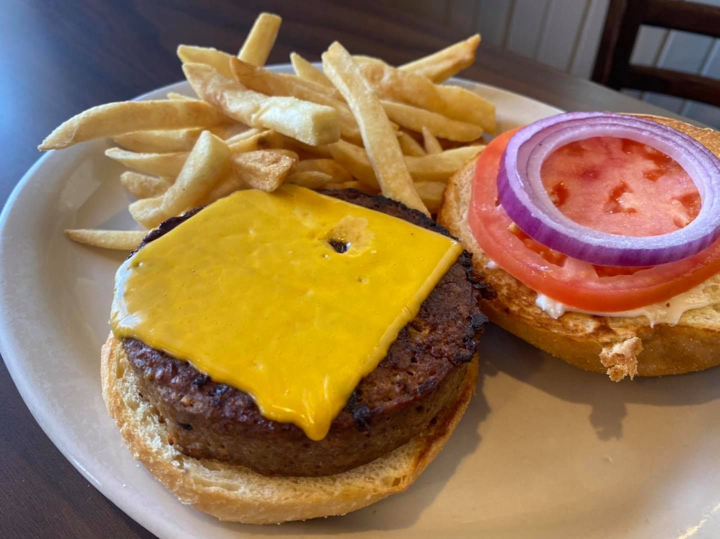 Burger with cheese, tomato, red onion, and fries on a plate.