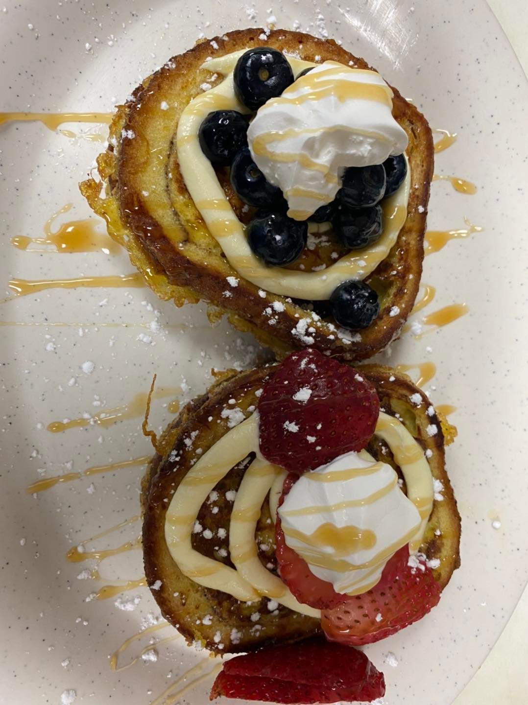 Two pieces of French toast topped with cream, berries, whipped cream, and syrup.