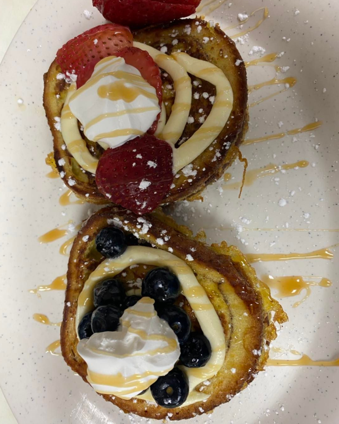 Two slices of French toast topped with whipped cream, berries, and drizzled sauce on a white plate.