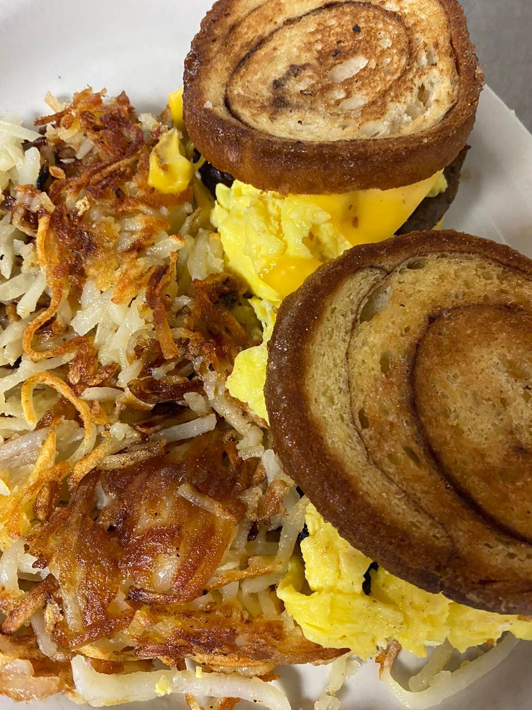Breakfast plate: egg sandwich on toasted swirl bread, side of hash browns.