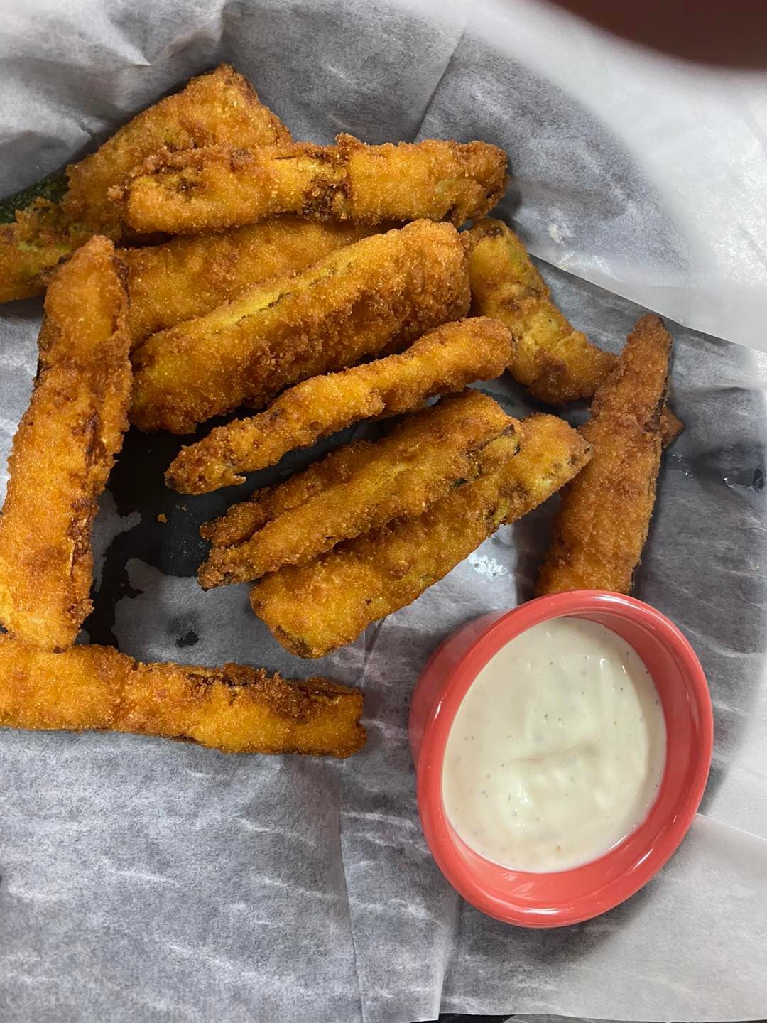Fried zucchini sticks and a small bowl of white dipping sauce, on a paper-lined plate.