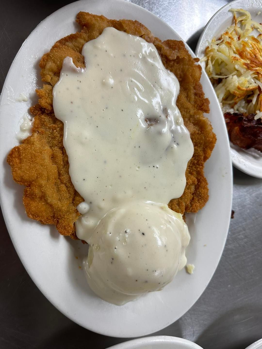 Breaded, fried meat covered in cream gravy and mashed potatoes on a white plate.
