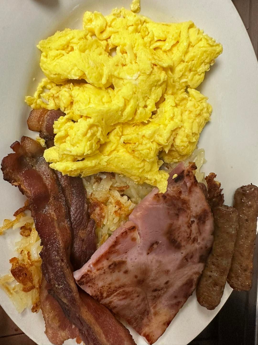 Scrambled eggs, bacon, ham, sausage, and hash browns on a plate.