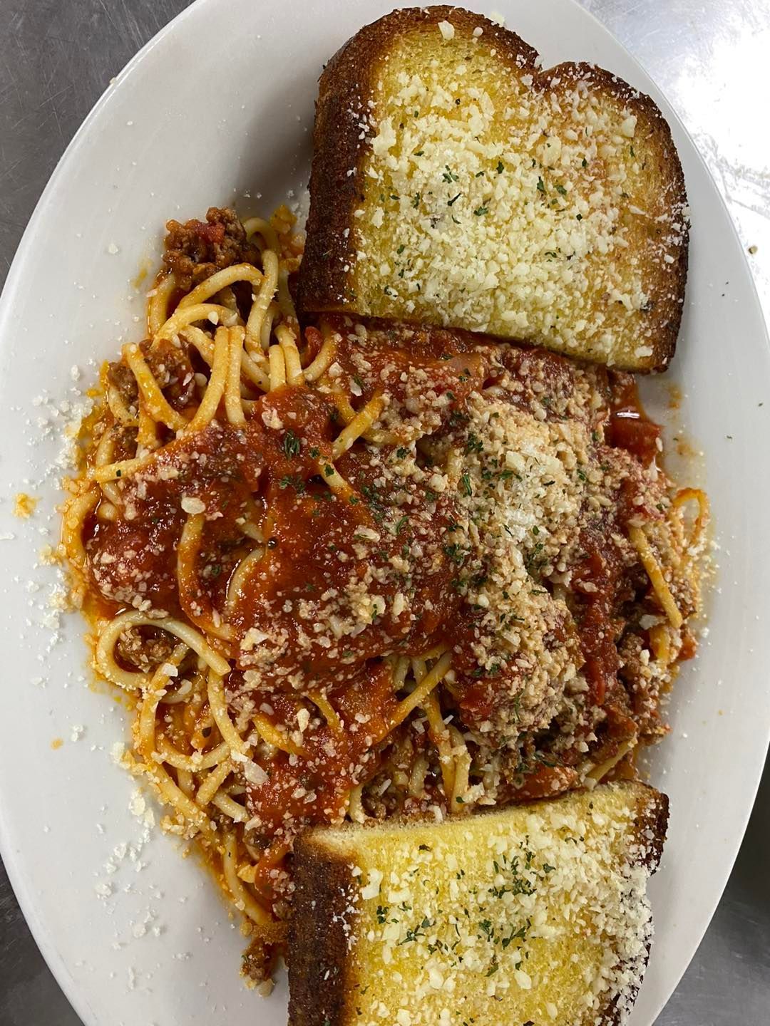 Spaghetti with meat sauce and garlic bread on a white plate, topped with parmesan cheese.