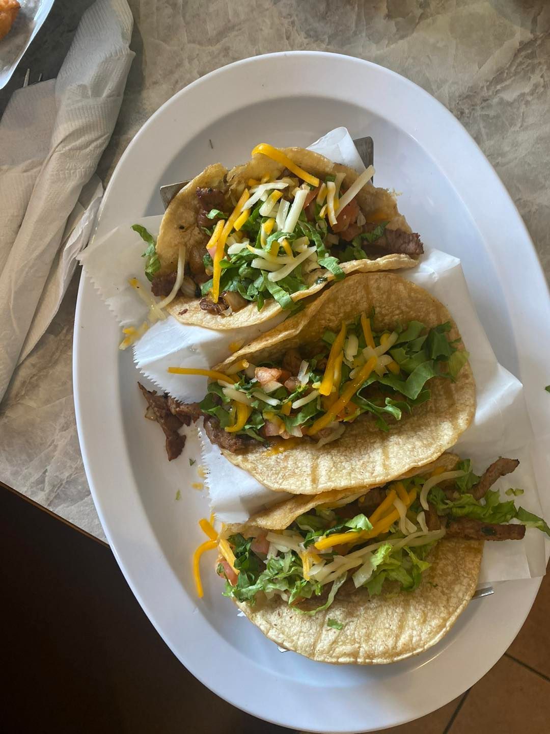 Three tacos on a white plate with lettuce, cheese, and meat.