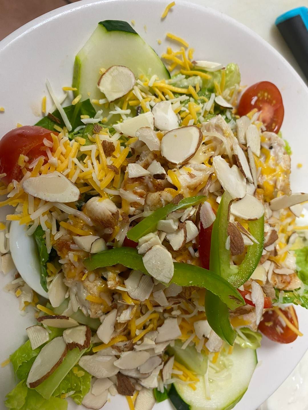 Salad with sliced cucumbers, tomatoes, cheddar cheese, almonds, and green bell pepper.