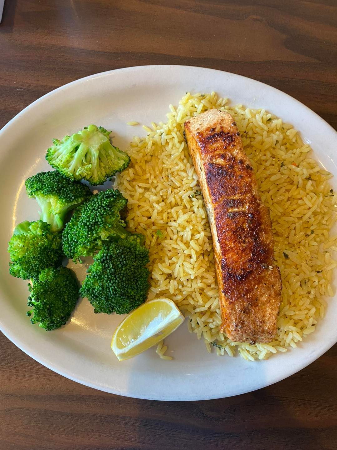 Salmon filet, rice, and broccoli on a plate with a lemon wedge.