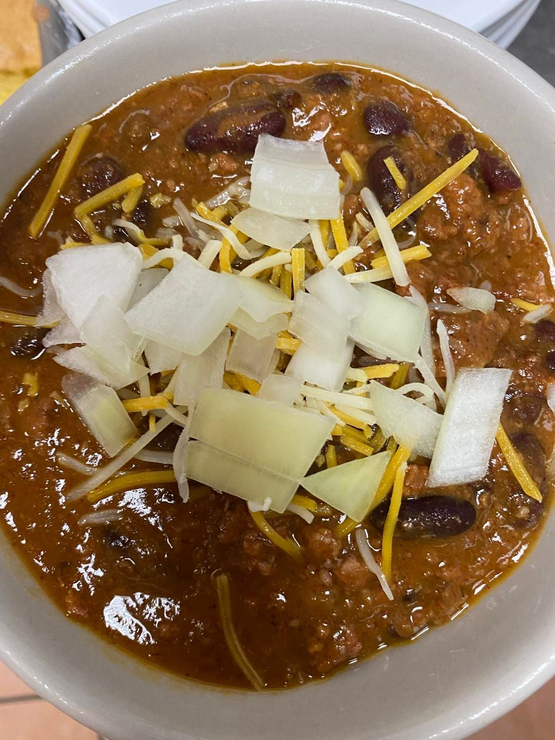 Bowl of chili topped with shredded cheese and chopped onions.