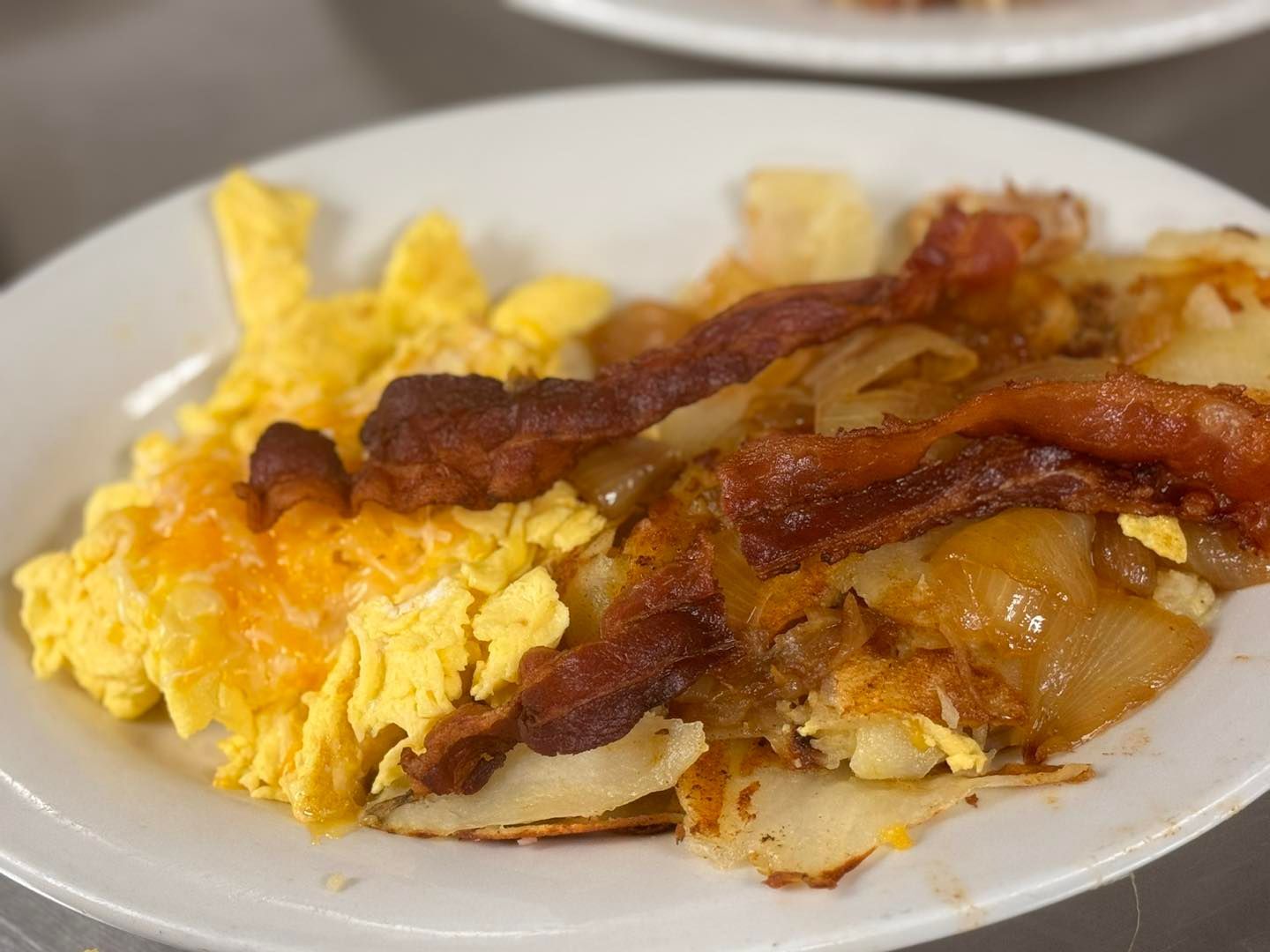 Scrambled eggs with cheese, bacon, and potatoes on a white plate.