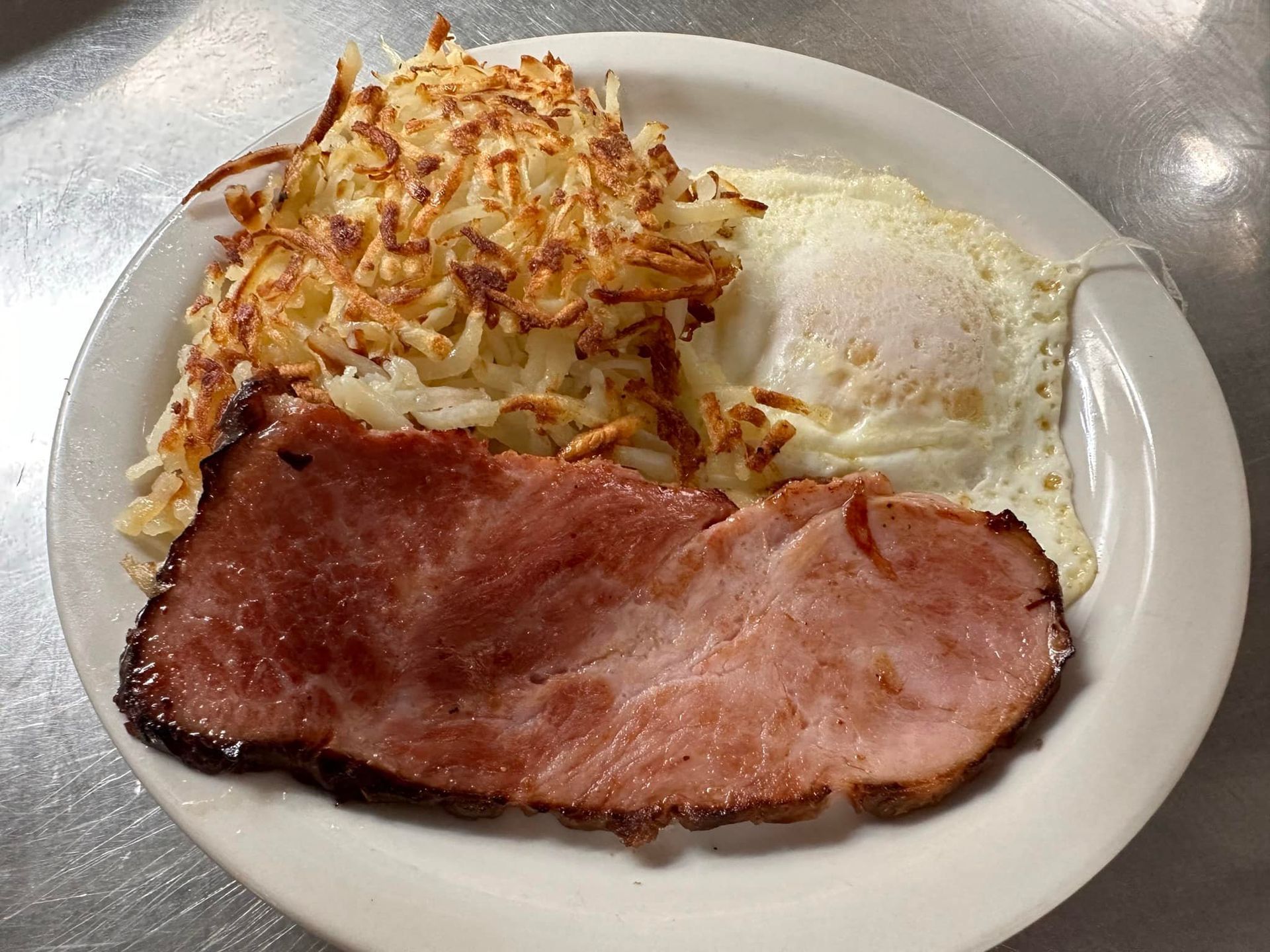 Plate of breakfast: ham, hash browns, and a fried egg.