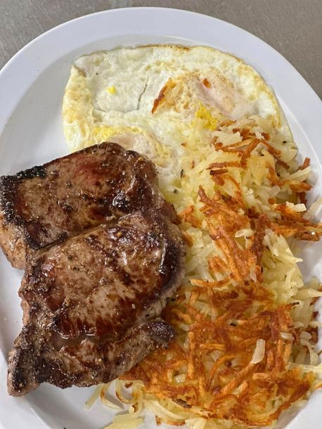 Steak, fried egg, and hash browns on a white plate.