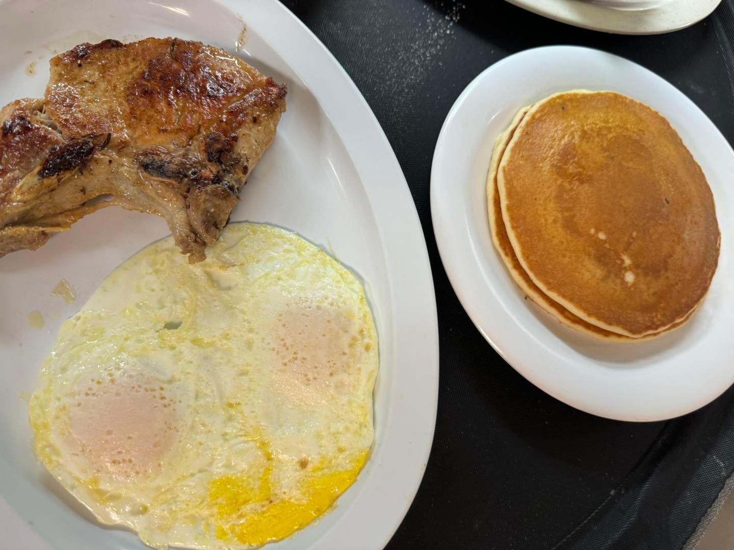 Fried eggs, chicken quarter, and pancakes on white plates.