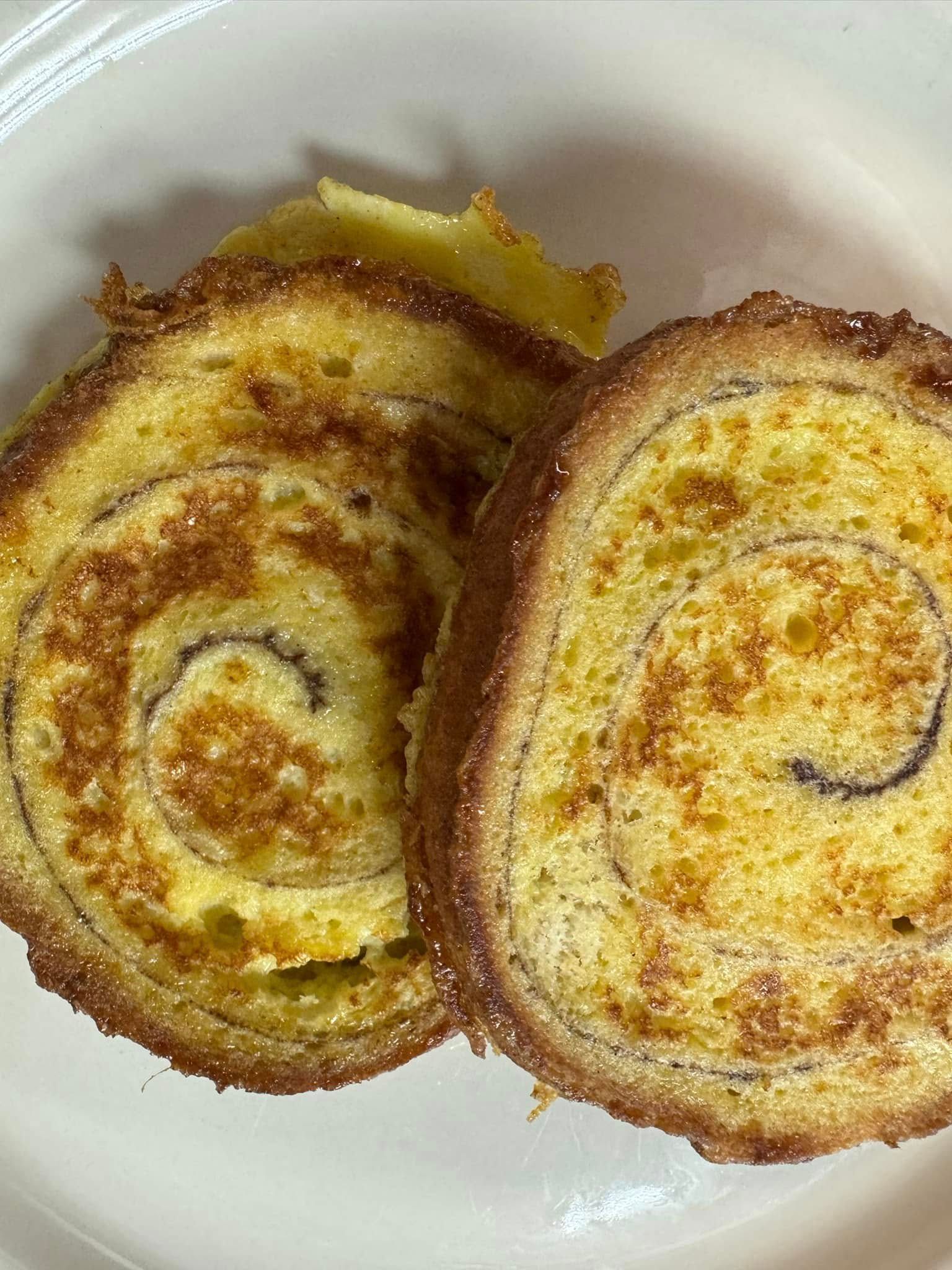 Two slices of a cinnamon roll, spiral design, on a white plate.