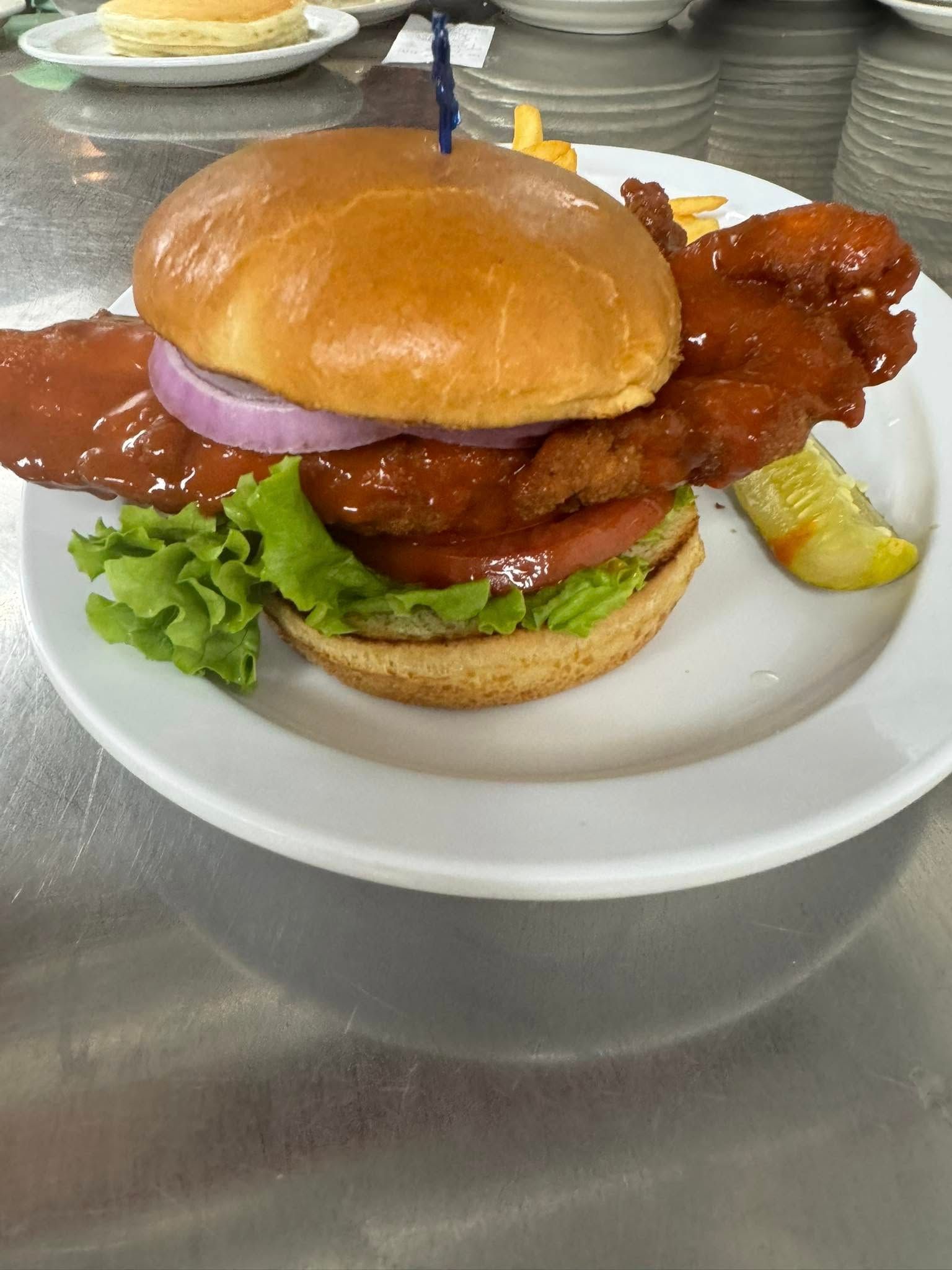 Chicken sandwich on a white plate, with lettuce, tomato, red onion, and pickle.