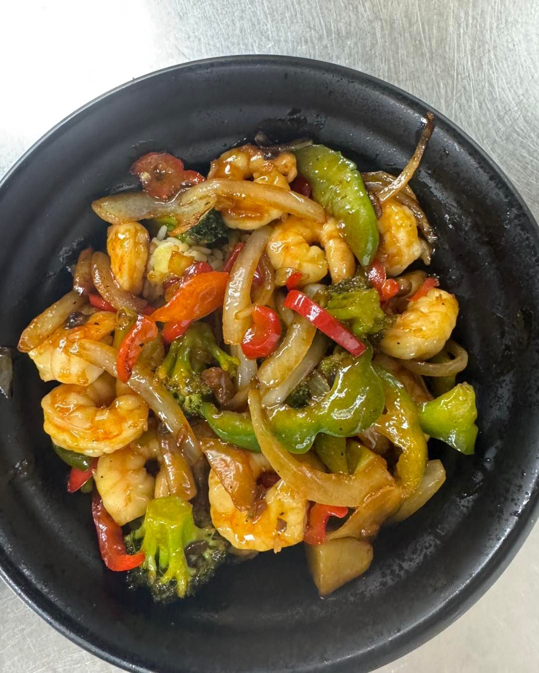 Stir-fry with shrimp, onions, bell peppers, and broccoli in a black bowl.
